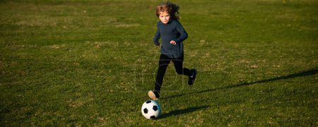 Téléchargez les photos : Un gamin de foot jouant au football. Enfant garçon jouer au football sur le terrain extérieur. Les enfants marquent un but au match de football. Le jeune garçon donne un coup de pied au ballon de foot. Joueur de football en mouvement, garçon en mouvement, bannière - en image libre de droit