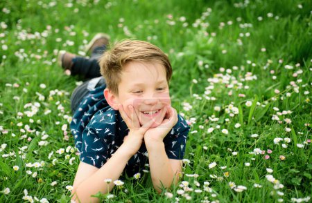 Carefree smiling boy lying on flower field. Cute kid child enjoying on lawn and dreaming