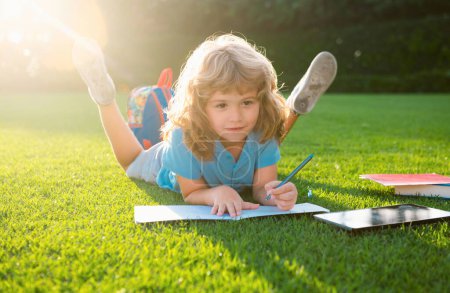 Téléchargez les photos : Enfant se détendre pendant les vacances. Enfant avec écriture au crayon sur carnet sur fond d'herbe. Nerd petit génie, éducation et concept d'apprentissage intelligent - en image libre de droit