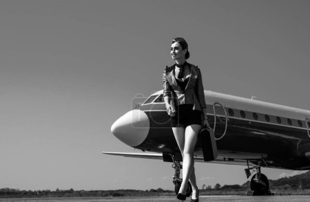 Téléchargez les photos : Aéroport et hôtesse de l'air charmante sur fond d'avion bleu. Portrait de charmante hôtesse en uniforme bleu. Femme et avion commercial. Toute la longueur de l'hôtesse de l'air debout par avion à réaction - en image libre de droit