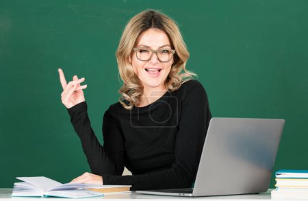 Foto de Profesora joven con el dedo en la mano en la lección en la pizarra en el aula. Profesor señalando, profesor mostrando a bordo - Imagen libre de derechos