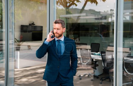 Téléchargez les photos : Portrait d'un homme d'affaires debout dans un bureau utilisant un smartphone parlant au téléphone - en image libre de droit