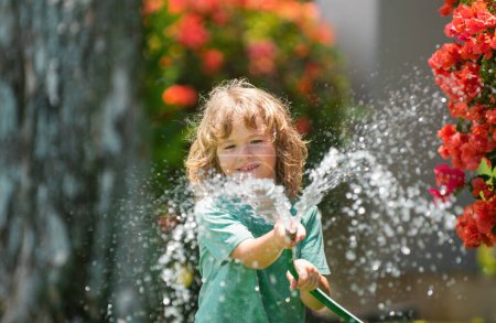 Photo for Cute little boy watering flowers in the garden at summer day. Child using garden hose. Funny kid watering plants in the yard garden - Royalty Free Image