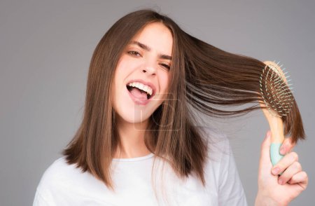 Close up portrait of happy beautiful girl with shiny hair with comb. Attractive smiling woman brushing hair