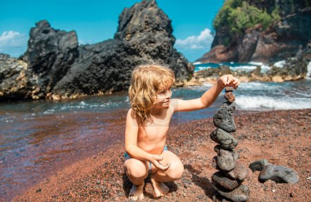 Téléchargez les photos : Enfant avec des pierres zen sur la plage de la mer, méditation, spa et harmonie. Calme concept d'équilibre. Les enfants jouent sur la plage - en image libre de droit