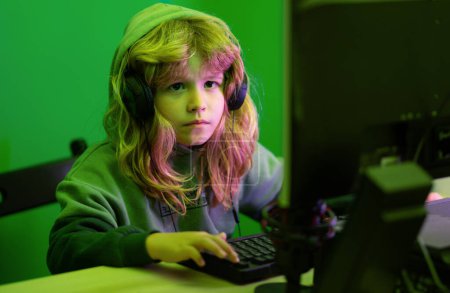 Téléchargez les photos : Enfant apprenant en ligne la nuit, en utilisant un ordinateur de bureau dans le salon à la maison. Enfant jouant à des jeux informatiques ou étudiant sur ordinateur PC. Gamer enfant la nuit néon éclairage - en image libre de droit