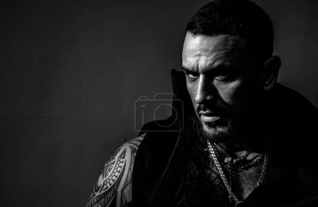 Man suppressing anger. Sexy fashion portrait of a hot male model in stylish leather jacket with accessories, muscular body posing in studio. Masculinity concept