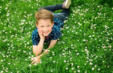 Happy carefree boy lying on grass lawn. Cute kid child enjoying on field flower and dreaming