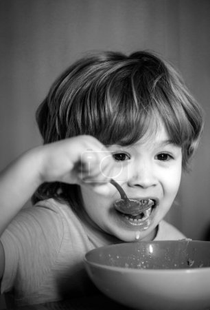 Foto de Cuidado de niños. Un niño desayunando en la cocina. Comida y bebida para niños. Niño pequeño - ecología Concepto de comida. Un chico lindo está comiendo. Niño sentado en la mesa y comiendo bocadillos de leche - Imagen libre de derechos