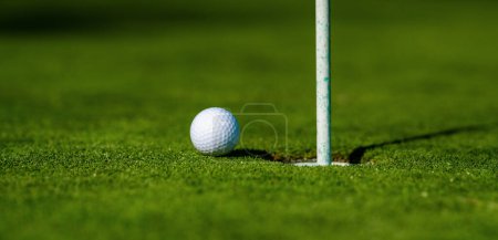 Téléchargez les photos : Boule de golf sur lèvre de tasse sur fond d'herbe. Trou de golf - en image libre de droit