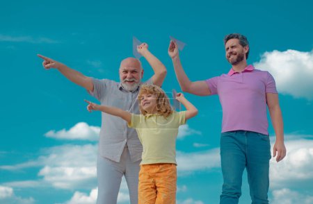 Foto de Abuelo padre e hijo jugando con avión de papel al aire libre en el cielo. Familia feliz. Tres generaciones de hombres. Feliz infancia. - Imagen libre de derechos