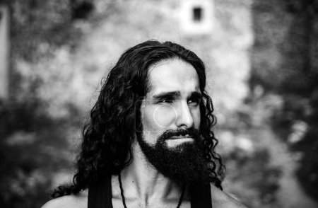 Sad frustrated man with long dark wavy hair and beard looking far away. Portrait of handsome man with disappointed face. Middle-aged sexy man with long hairstyle