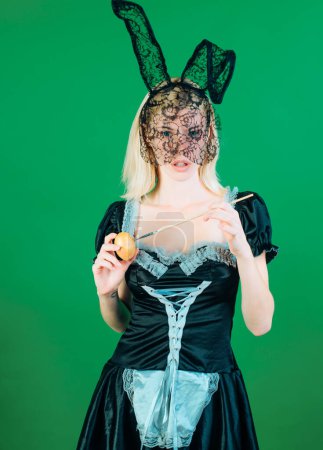 Téléchargez les photos : Jolie jeune femme portant un masque noir lapin de Pâques sur fond vert, isolé. Femme surprise. Pâques de lapin. Belle blonde sensuelle - en image libre de droit
