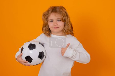 Foto de Niño niño mantenga pelota de fútbol clásico aislado en el estudio amarillo. Niño sosteniendo pelota de fútbol en el estudio. Chico jugando con la pelota. Deporte, hobby de fútbol para niños. Pequeño jugador de fútbol posando con pelota de fútbol - Imagen libre de derechos
