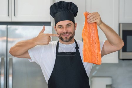 Téléchargez les photos : Chef avec filet de saumon de viande crue sur la cuisine. Chef en uniforme en cuisine. Beau chef en uniforme avec chapeau de chef cuisinier filet de saumon de poisson cru dans la cuisine - en image libre de droit