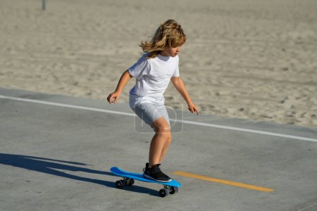 Child skateboarder ride on skateboard in park. Young smiling teenager boy riding on modern cruiser skateboard, urban background