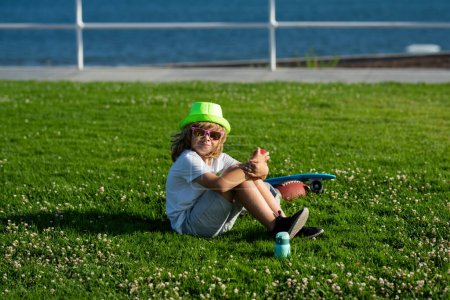 Téléchargez les photos : Détendez-vous au parc d'été. Enfant assis sur l'herbe verte en plein air. Pique-nique d'été sur herbe avec enfants. Concept de mode de vie sain - en image libre de droit