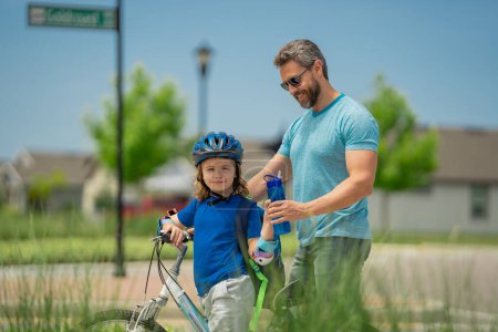 Happy family. Father and son riding bike in park. Child in safety helmet with father riding bike in summer day. Father teaching son riding bike. Fatherhood. Support parent. Fathers day. Child care
