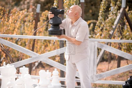 Téléchargez les photos : Senior jouant aux échecs sur un grand échiquier dans le parc. Jeu d'échecs pour vieux grand-père, grand-père pensionné, concept de retraité. Homme d'âge moyen loisirs de plein air - en image libre de droit