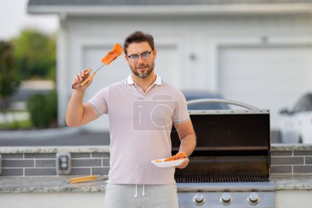 Photo for Man cooking salmon fillet on barbecue in the backyard of the house. Handsome man preparing barbecue. Barbecue chef master. Cook preparing delicious grilled barbecue food, bbq salmon fillet - Royalty Free Image