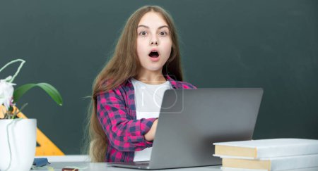 Foto de Sorprendido adolescente estudiante de la escuela con el ordenador portátil en la escuela. Estudiante adolescente trabajando en el ordenador portátil en el aula. Niña usando el ordenador portátil, estudiar en línea en el ordenador. Concepto de educación en el hogar. Lección escolar - Imagen libre de derechos
