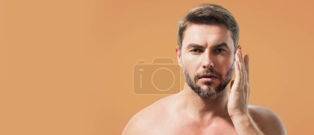 Close up beauty portrait of half naked satisfied young man after facial cream. Attractive brunet guy touching skin. Men model face with beard and modern haircut. Banner for header, copy space