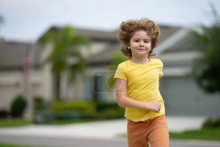Foto de Un chico corriendo en la calle de verano. A los niños les gusta correr. Un niño corriendo por la calle del vecindario. Los niños corren por la carretera de la ciudad americana. Niño corriendo en el parque. Deportes y fitness, hacer ejercicio para niños - Imagen libre de derechos