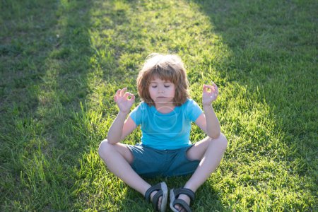 Foto de Niño lindo meditando en el parque de primavera. Concepto de libertad. Meditación pacífica de los niños. Niño haciendo yoga en el parque matutino - Imagen libre de derechos