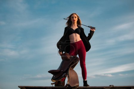 Photo for A horsewoman. Cowgirl hold saddle and whip. Equestrienne horsewoman. American cowboy style. Cowgirl woman in countryside. Horsewoman jockey. Jockey Equestrienne equipment - Royalty Free Image