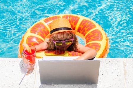 Photo for Kid drink summer cocktail and using laptop in swimming pool. Funny little business man works for a laptop in pool water. Remote work. Little freelancer. Business and summer. Little blogger - Royalty Free Image