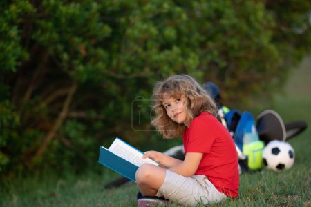 Téléchargez les photos : Un enfant a lu un livre. École élémentaire de plein air. Éducation préscolaire des enfants. Les devoirs d'été. Petite étudiante en plein air. Les enfants et le concept éducatif. Enfant pique-nique dans le parc d'été - en image libre de droit