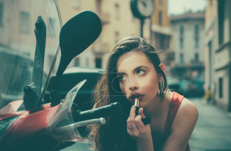 Photo for Sensual businesswoman, successful business woman. Applying makeup on street. Sexy fashion girl with red lips put lipstick looking in a mirror of motorcycle - Royalty Free Image