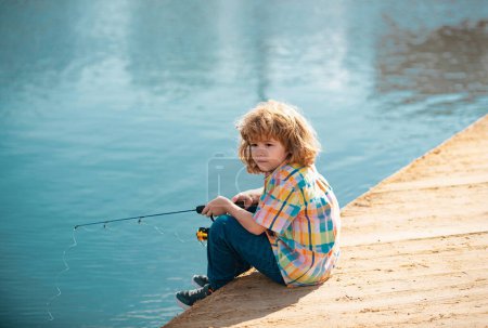 Téléchargez les photos : Un jeune pêcheur. Pêche des enfants au bord de la rivière, activités de plein air estivales. Petit garçon pêchant au bord de la rivière avec canne - en image libre de droit