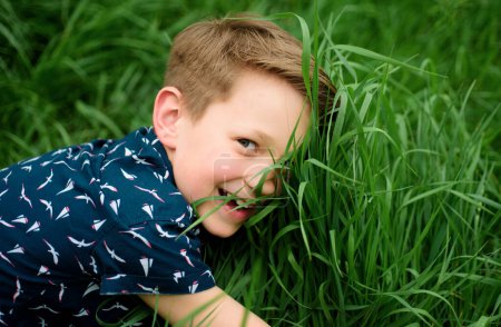 Niño sonriente con fondo de hierba. Lindo chico disfrutando en el campo. Unidad con la naturaleza