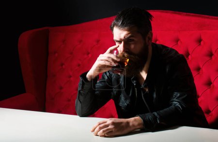 Bearded man drinking whisky, whiskey or cognac brandy. Hipster brutal man drinker alcoholic with alcoholism problem, alcohol abuse addiction concept. Drunken man behavior