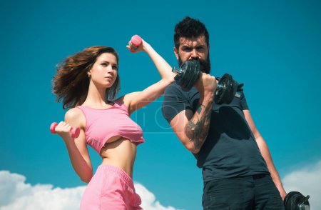 Photo for Fit sexy couple on sky background with dumbbells. Fitness concept. Sports couple training with dumbbell. Healthy coupl life style. Fitness sexy models pumping up arm with dumbbell - Royalty Free Image