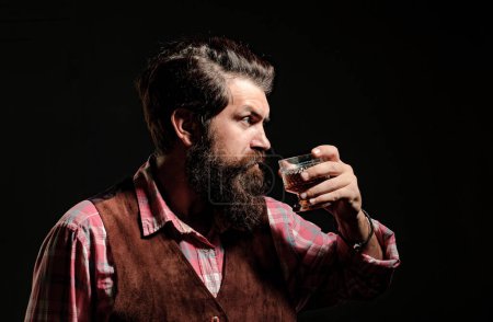 Un hombre elegante que sufre de alcoholismo bebiendo whisky. Un hombre guapo barbudo sosteniendo un vaso de whisky. Hombre atractivo en el bar de whisky