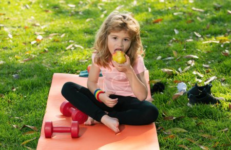 Téléchargez les photos : Une saine alimentation sportive pour les enfants. Enfant garçon après le sport assis sur le tapis de sport boire de l'eau et manger des pommes - en image libre de droit