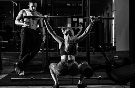 Foto de Mujer entrenando con barra en el gimnasio. Entrenador muscular hombre mujer de entrenamiento con barra. Instructor de fitness entrenador personal - Imagen libre de derechos