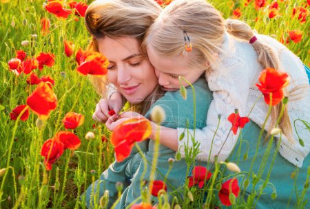 Foto de Madre e hija abrazándose en un prado de amapolas. Mamá y niña descansando en el campo con flores de amapola. Madre e hija en primavera - Imagen libre de derechos