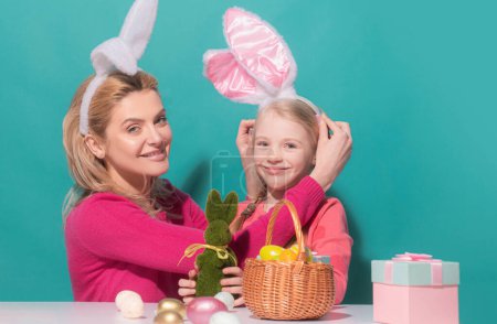 Mother and child daughter celebrating Easter. Cute little girl with funny face in bunny ears laughing, smiling and having fun isolated on blue