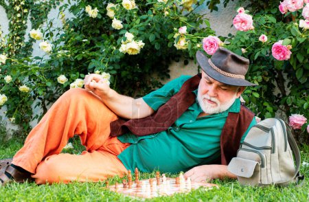 Foto de Viejo hombre mayor en jardín de primavera o patio trasero con ajedrez. Concepto de hobby. Feliz vejez - Imagen libre de derechos