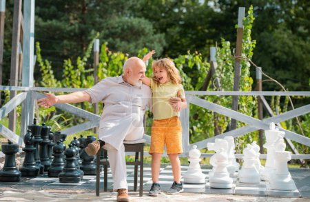 Photo for Child boy and grandfather playing chess on big chess board. Spending time together with granddad. Family Relationship Grandfather and child - Royalty Free Image