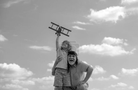 Photo for Child boy and grandfather with toy plane over blue sky and clouds background. Men generation grandfather and grandson playing outdoors - Royalty Free Image