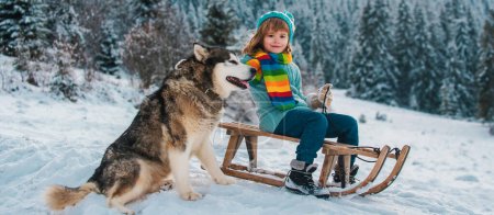 Téléchargez les photos : Enfant garçon avec chien s'amusant avec un traîneau en hiver. Enfants avec chien - en image libre de droit
