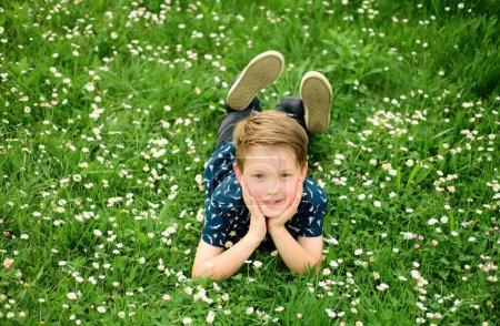 Bonne enfance. Garçon souriant couché sur l'herbe. Enfant de printemps appréciant sur la pelouse de fleurs de champ. Concept de rêve