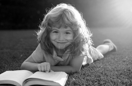 Foto de Retrato de niño feliz con libro en el parque. Educación temprana para niños. Niño pequeño leer libro en el jardín. tarea de vacaciones de verano. Estudiante de preescolar al aire libre. Lindo niño de la escuela primaria - Imagen libre de derechos