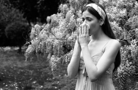 Girl with nose allergy sneezing. Polen illnes symptom concept. Woman allergic to blossom during spring blooming tree outdoor
