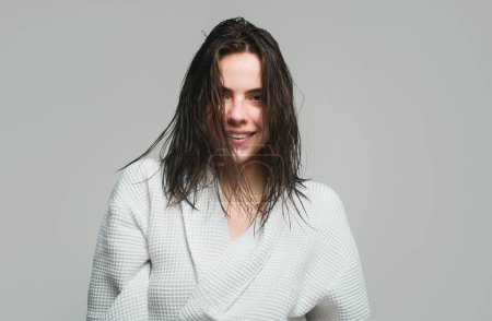 Foto de Feliz retrato de mujer joven sonriente en albornoz. Modelo femenino de mañana con el pelo mojado. Cuidado del cabello y belleza. Rutina matinal - Imagen libre de derechos
