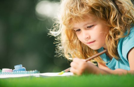 Téléchargez les photos : Peinture pour enfants avec peinture couleur et pinceau dans le parc en plein air. Loisirs d'enfants, enfance heureuse. Elève enfant apprenant la peinture - en image libre de droit